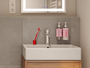 Um banheiro com pia branca, porta-escovas de dentes vermelho e duas embalagens de loção.
