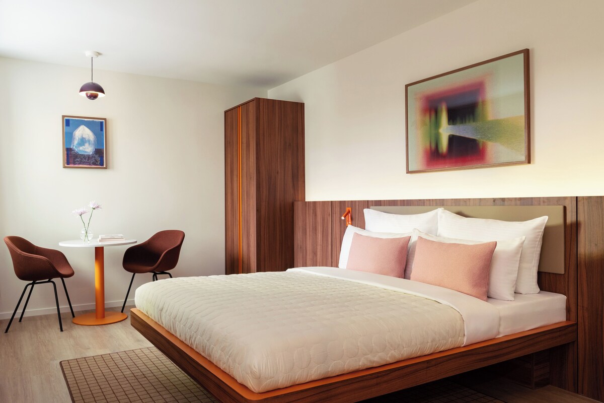 Een moderne hotelkamer met een groot bed, een kleintje tafeltje met stoelen en een schilderij aan de muur.