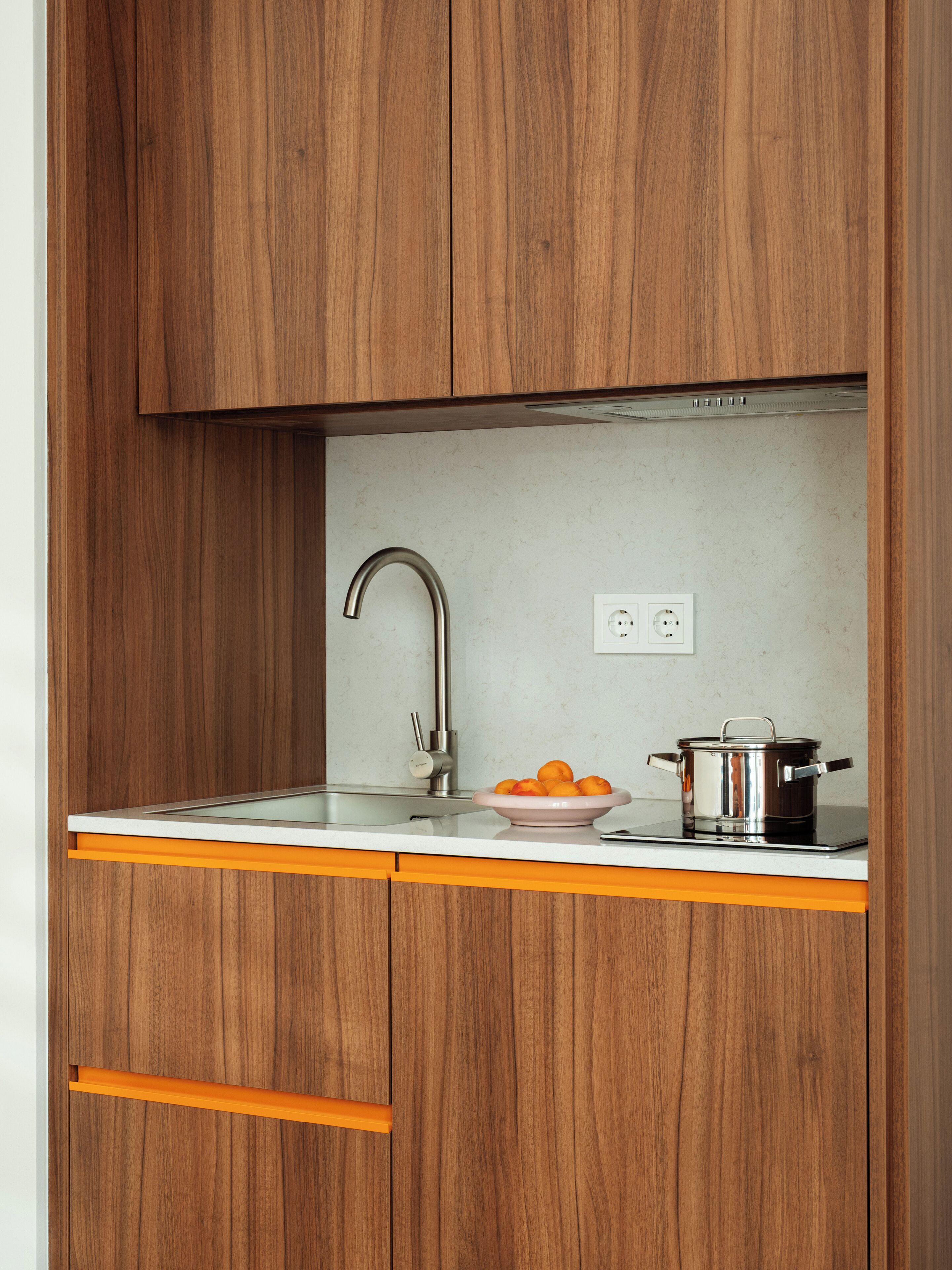 Una cocina con armarios de madera, un lavamanos de acero inoxidable y una encimera con una olla y naranjas.