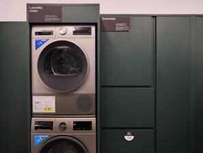 Ein Waschraum mit einer Bosch T1 Waschmaschine und einer HOS Waschmaschine, einem Schild für Wäschebedarf und einem Spender für schmutzige Handtücher.
