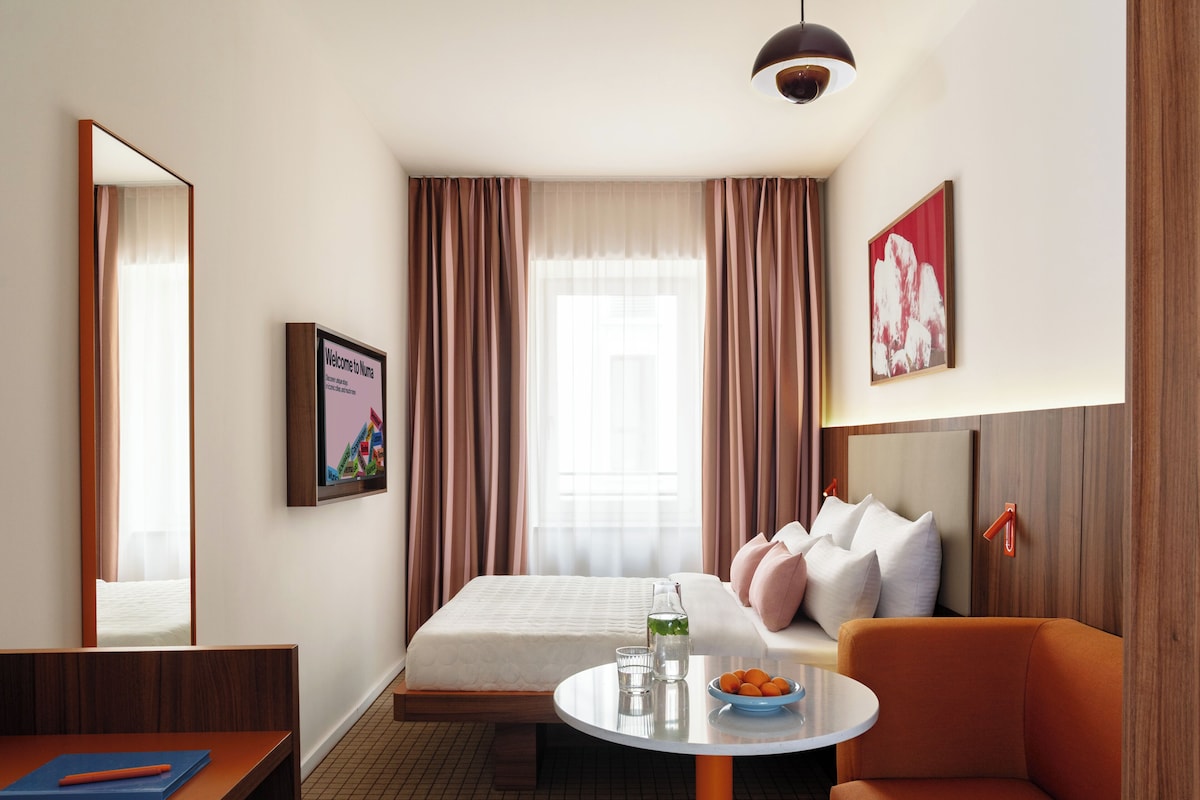 Een hotelkamer met een bed, een bank, een tafel met een schaal fruit, een nachtkastje, een spiegel en een welkomstbord.