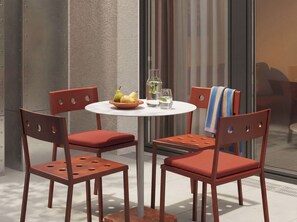Mesa com cadeiras, uma tigela de fruta e copos em um terraço.