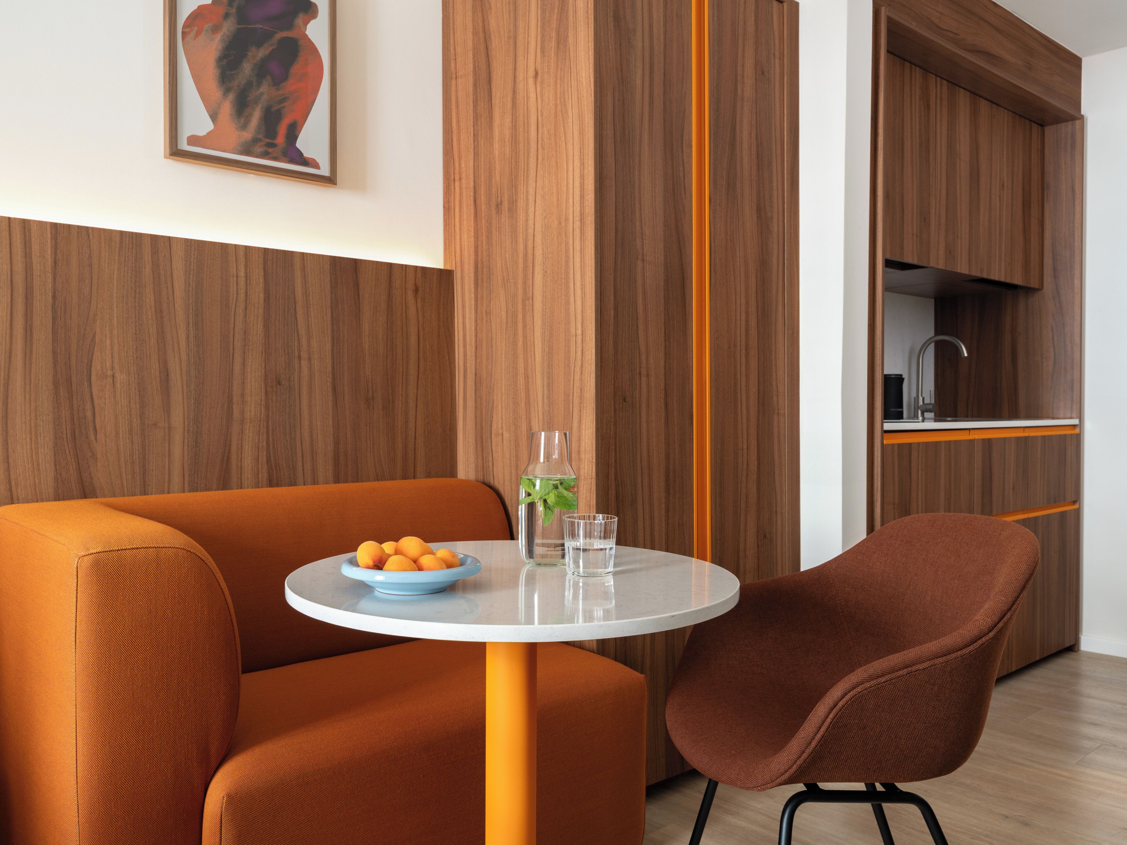 Una habitación moderna con una mesa redonda, sofá naranja y una cocina con armarios de madera.
