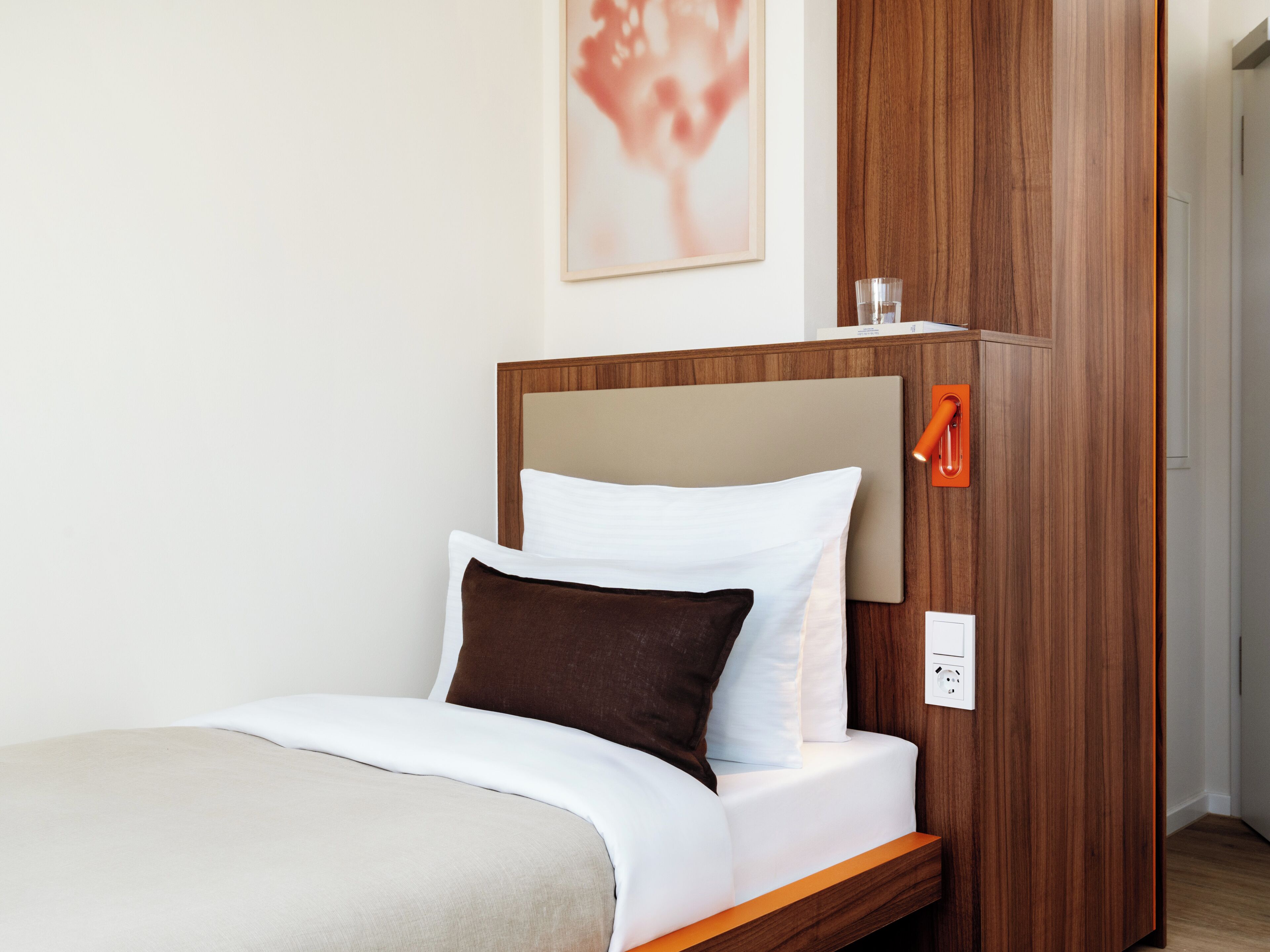 Habitación de hotel con cama, mesita de noche, lámpara de pared y toma de corriente.