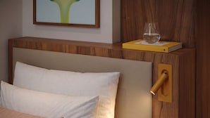 Un dormitorio con cabecera de madera, mesita de noche con vaso y libro, y un cuadro en la pared.