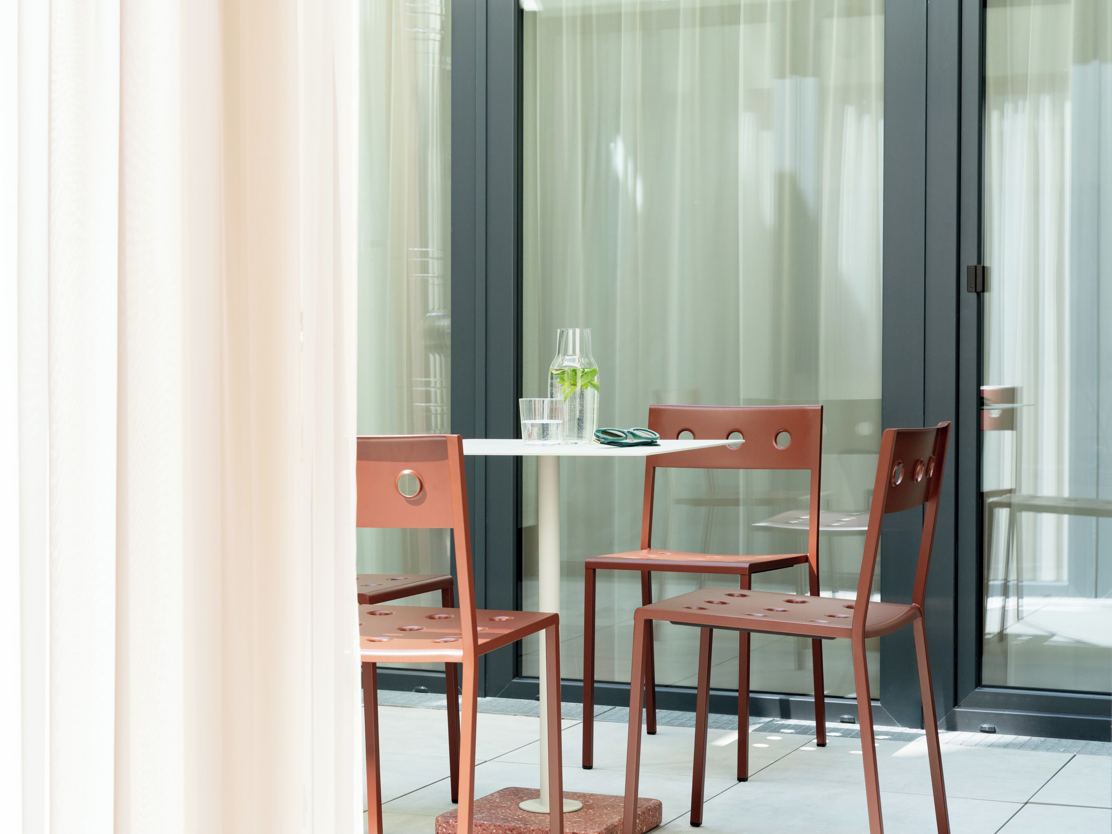 A modern outdoor seating area with a table and two chairs, a glass door, and a view of the street.