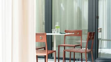 A modern outdoor seating area with a table and two chairs, a glass door, and a view of the street.
