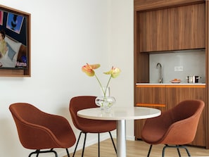 Cocina moderna con armarios de madera, encimera blanca y una mesa redonda de comedor con dos sillas marrones.