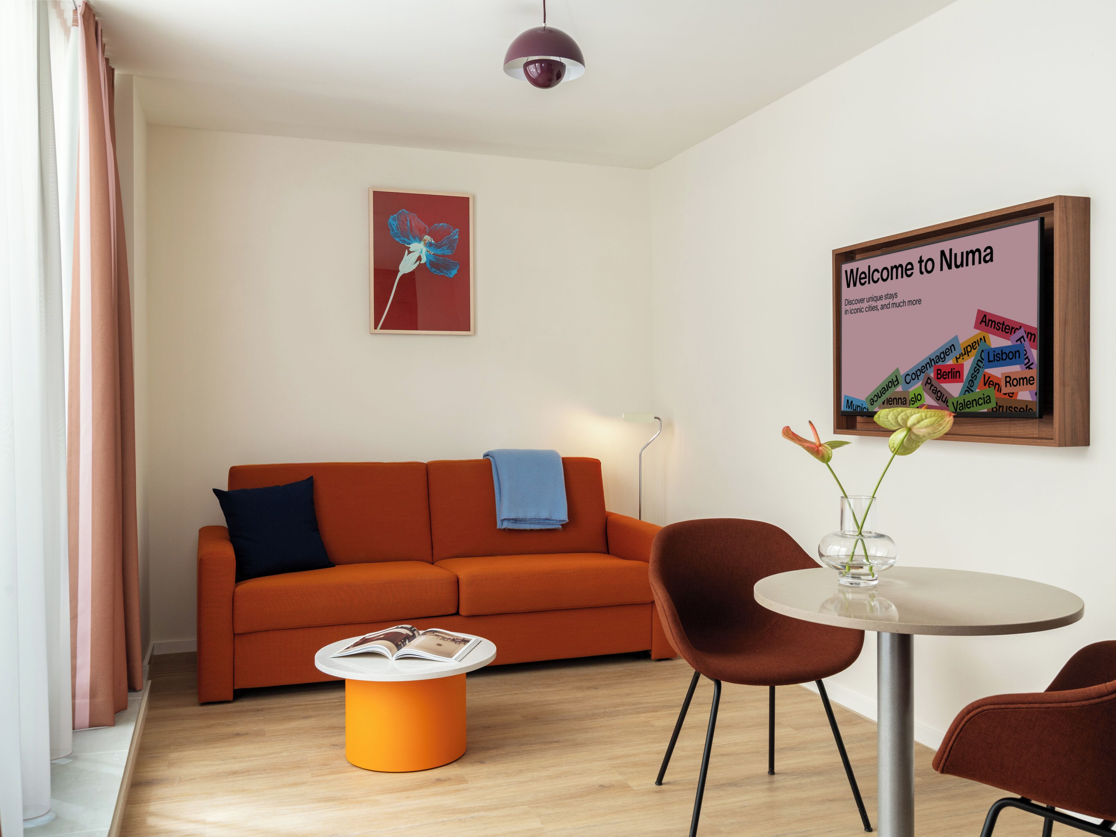 A modern living room with a sofa, a coffee table, and a round table with chairs. There is a framed welcome sign and a wall art piece.