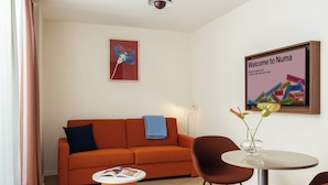 Una sala de estar moderna con un sofá, una mesa de centro y una mesa redonda con sillas. Hay un letrero de bienvenida enmarcado y una obra de arte en la pared.