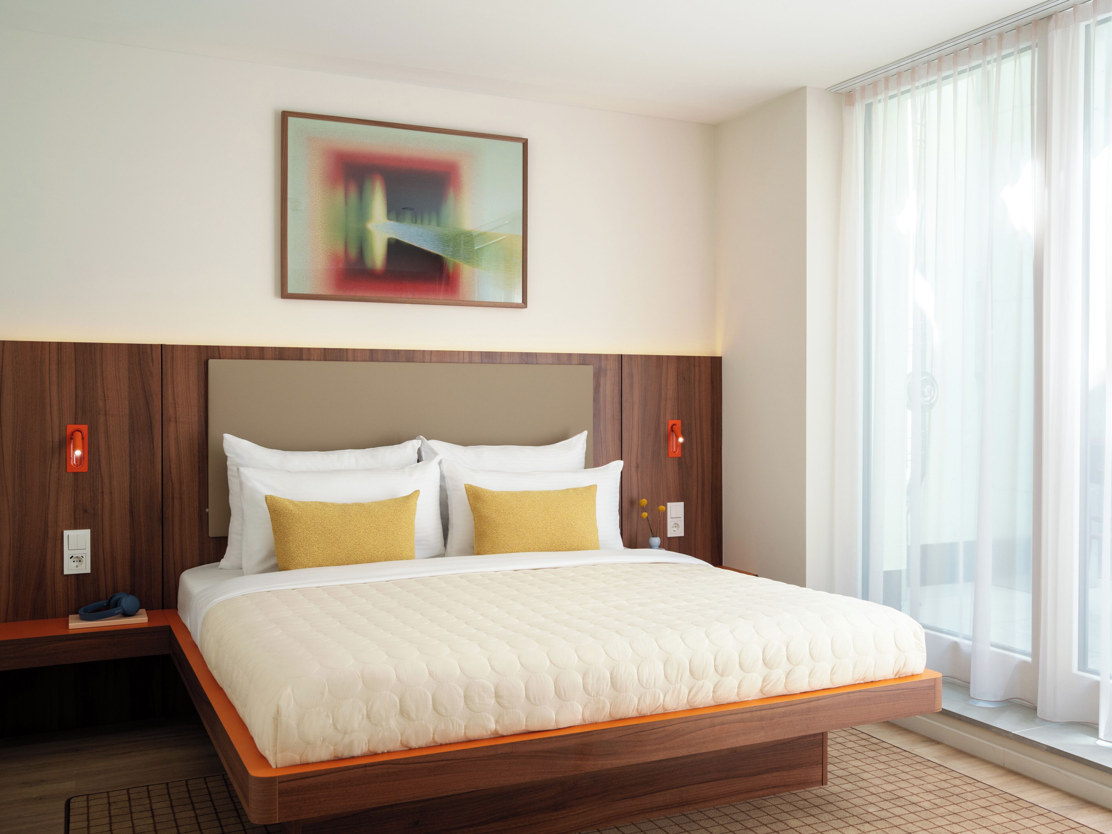 Habitación de hotel con cama, cabecero de madera, ropa de cama blanca y un cuadro en la pared.