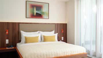 Habitación de hotel con cama, cabecero de madera, ropa de cama blanca y un cuadro en la pared.