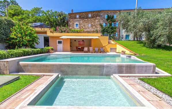 A swimming pool with a sun terrace, a stone building, and lush greenery.