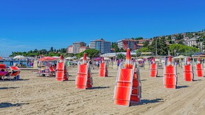 Una spiaggia con file di sedie arancioni, un cielo blu limpido e edifici sullo sfondo.