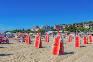A beach with rows of orange beach chairs, a clear blue sky, and buildings in the background.