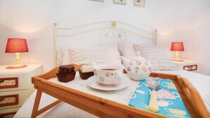 Un letto rifatto con cuscini e un vassoio con teiera, tazza e muffin. Due comodini con lampade e una parete con quadri.