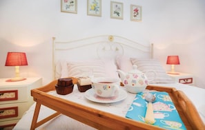 A neatly made bed with pillows and a tray with a teapot, cup, and muffin. There are two bedside tables with lamps and a wall with framed pictures.