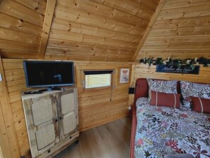Een houten cabin met een televisie, een klein raam, een bed met bloemenbeddengoed, en een bord boven het bed.
