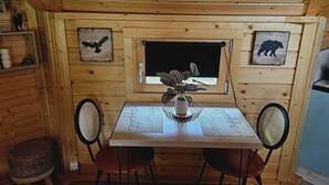 Interior d'una cabana de fusta amb taula de menjador, dues cadires, una finestra amb vistes i obra d'art penjada a la paret.