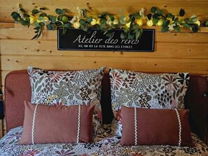 Ein Bett mit blumigem Bettbezug, zwei braune Kissen und ein Schild darüber mit der Aufschrift 'Atelier du rêve'.