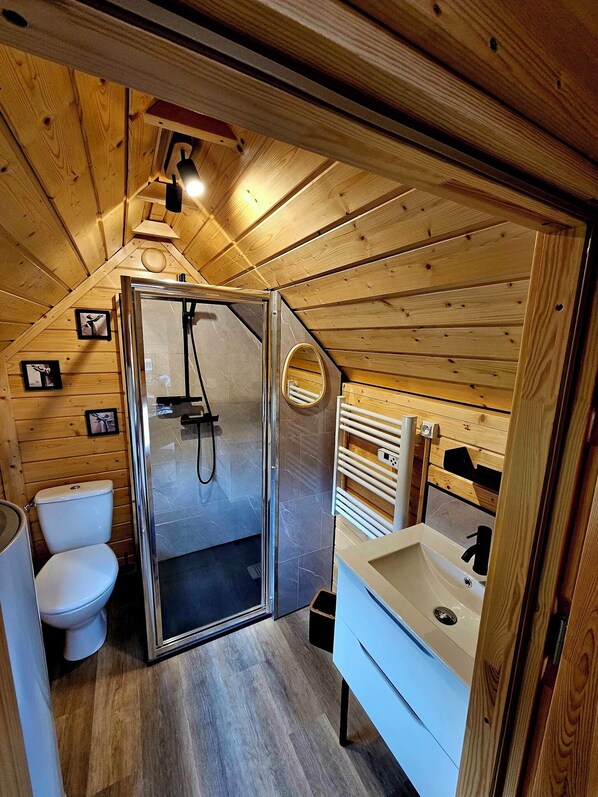 Ein Badezimmer einer Holzhütte mit Dusche, Toilette und Waschbecken.