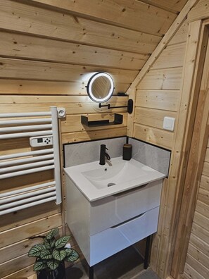 A compact bathroom with a white sink, a mirror, a towel rack, and a small potted plant.
