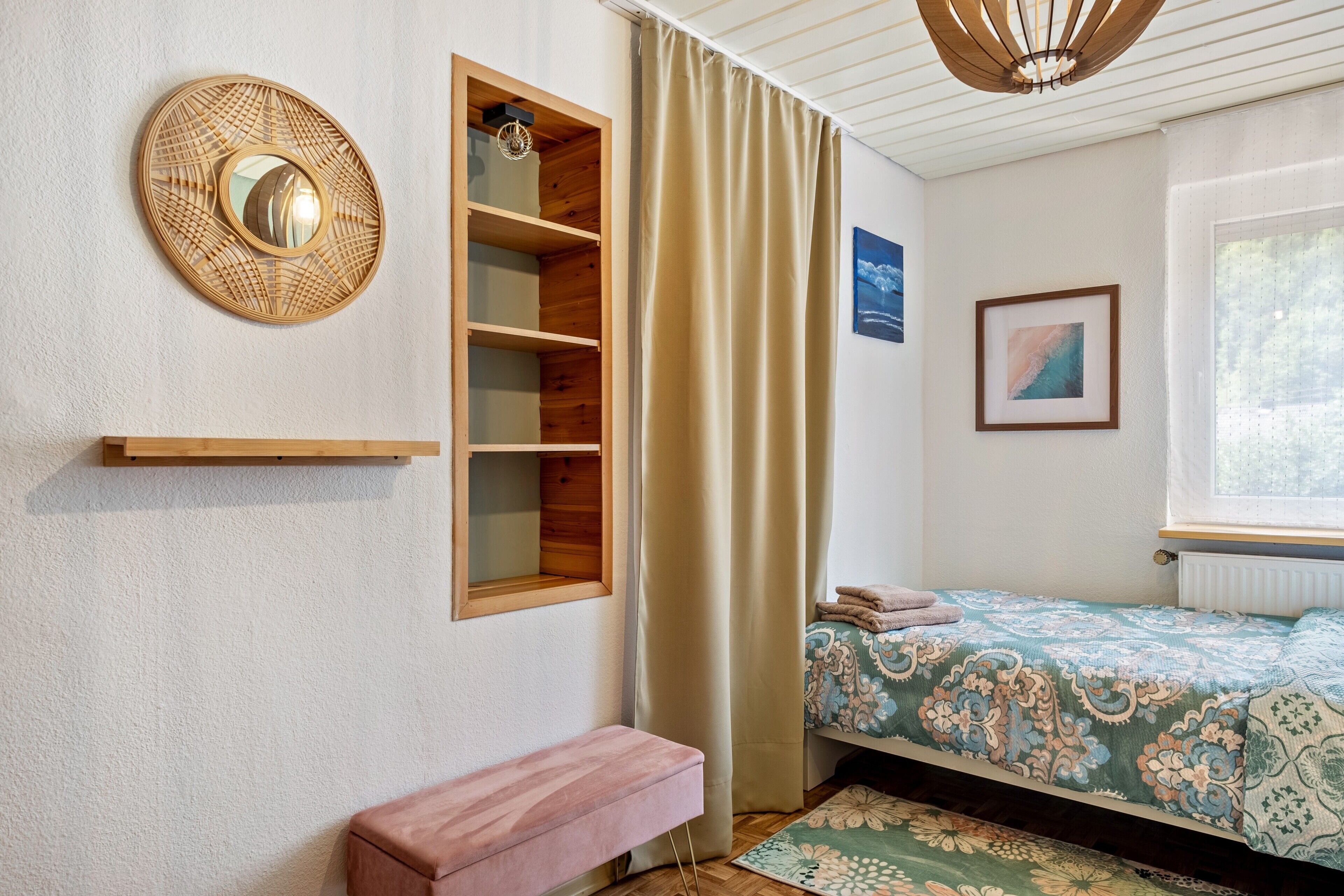 Een slaapkamer met een bed, een bankje, een plank, een spiegel en een raam.