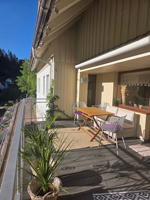 Um deck de madeira com mesa e cadeiras, um vaso de planta e uma janela com vista para casas.