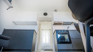 Une cuisine compacte dotée d’un four encastré, d’un petit coin repas avec une chaise et d’une fenêtre avec des rideaux.