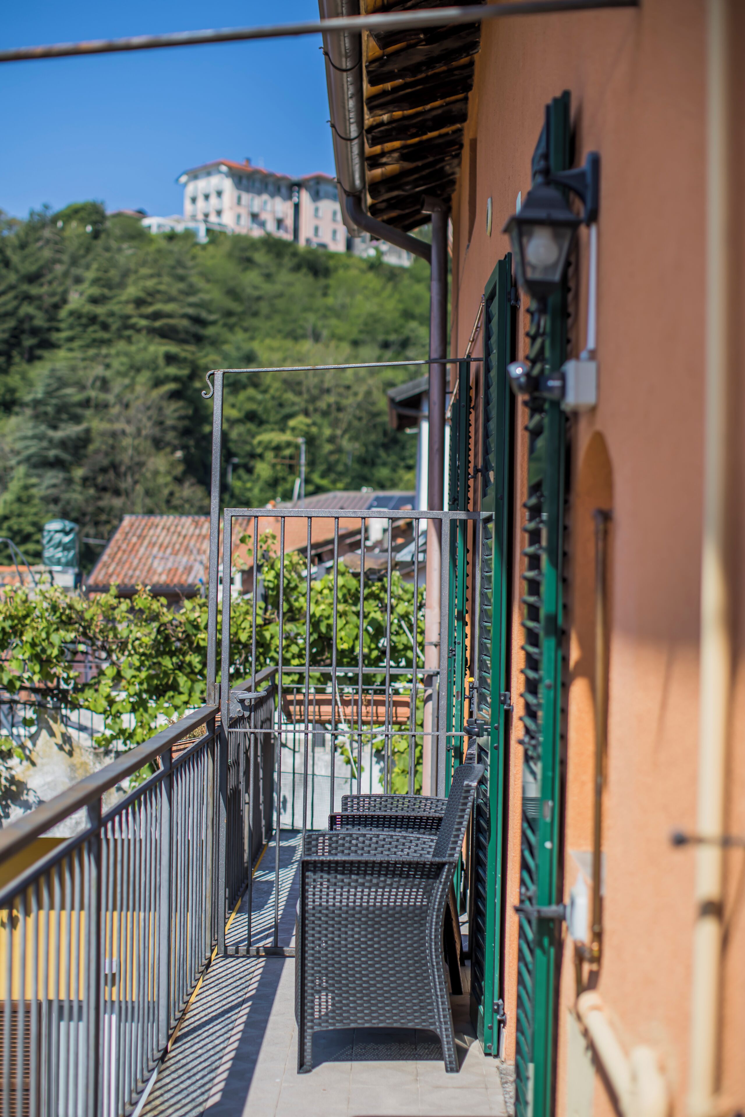 A balcony with a metal railing, a green door, and a view of buildings and greenery in the background.