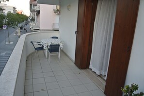 Ein Balkon mit Tisch, Stühlen, einer Tür und Blick auf die Straße.