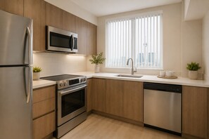 A modern kitchen with stainless steel appliances, wooden cabinets, a window with blinds, and a potted plant. - The Aeris Suites (Toronto)