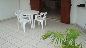 Eine kleine Terrasse mit weißem Tisch und Stühlen, einem Blumentopf und einer Tür, die zu einem Innenraum führt.