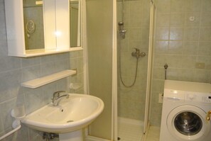 Une salle de bain équipée d’un lavabo, d’un miroir, d’une douche et d’un lave-linge.