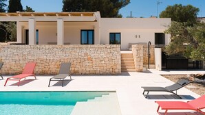 En modern villa med en stenmur, en swimmingpool och en uteplats med sittplatser.