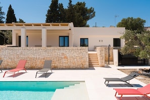 Eine moderne Villa mit Steinmauer, Schwimmbad und Außenbereich mit Sitzgelegenheiten.