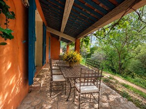 An outdoor patio with a table and chairs, surrounded by greenery and a covered area with blue shutters. - Villas between Provence and nature on the Château Roubine estate (Lorgues)