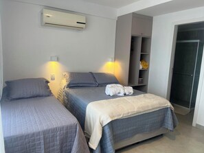 Quarto de hotel com duas camas, ar condicionado, guarda-roupa e chuveiro.