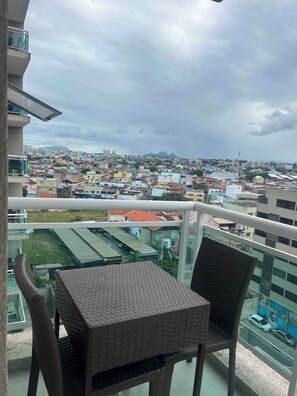 Varanda com móveis de vime, vista para um horizonte urbano e montanhas ao longe.