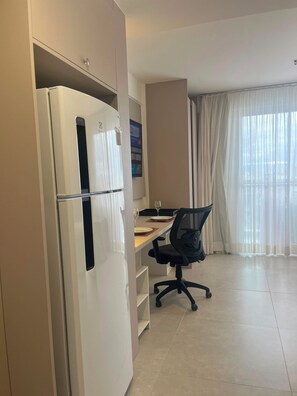 A modern kitchen with a built-in refrigerator, a dining area with a table and chairs, and a large window with sheer curtains. - NEW Fully Equipped Apartment in Imbetiba (Macaé)