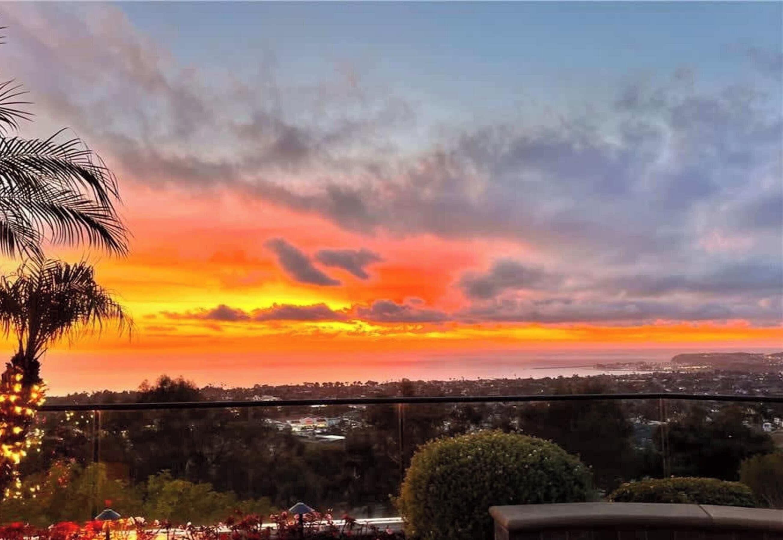 A sunset view from a balcony with palm trees and a distant cityscape.