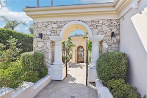 A stone archway leading to a building entrance, surrounded by well-maintained hedges and a clear sky.