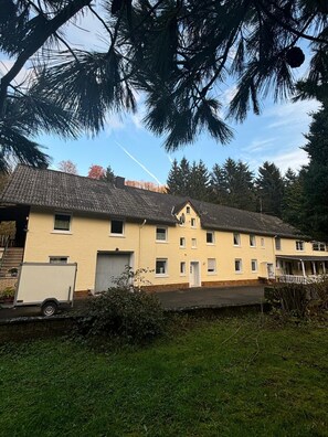 A two-story building with a tiled roof, a white door, and a small porch. - Relaxation in the Eifel - nature, peace and comfort for families, couples and dog lovers (Seffern)