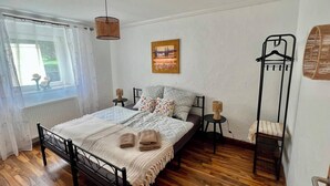 Een slaapkamer met een bed, nachtkastjes, een hanglamp, een raam met gordijnen en een kapstok aan de muur.