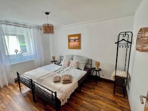 A bedroom with a bed, bedside tables, a hanging light fixture, a window with curtains, and a wall-mounted coat rack.