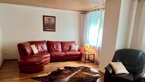 Een woonkamer met een rode leren bank, een zwarte leren fauteuil, een houten vloer en een groot bont tapijt.