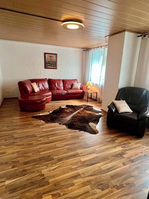 A living room with a red leather sofa, a black leather chair, a wooden floor, and a large fur rug.