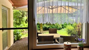Een kamer met een schuifdeur die uitkomt op een terras met rieten meubels en een tafel.