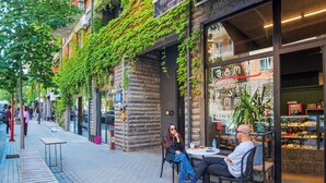An outdoor café with tables and chairs, a stone wall, and a building with a glass storefront. - HB apartments Politkovskaia (Tbilisi)