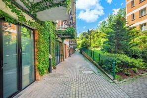A narrow brick-paved pathway flanked by buildings with green ivy and a metal fence. - HB apartments Politkovskaia (Tbilisi)